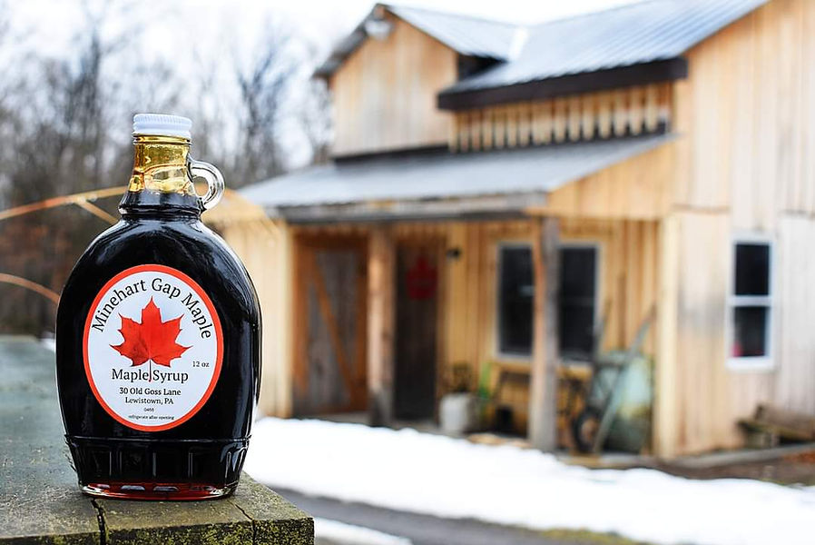 close up of minehart gap maple syrup in glass bottle in from of rustic building in pa