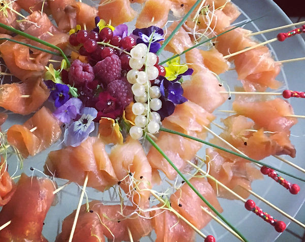 Plateau de saumon fumé disposé en rosace, fleurs comestibles et brochettes