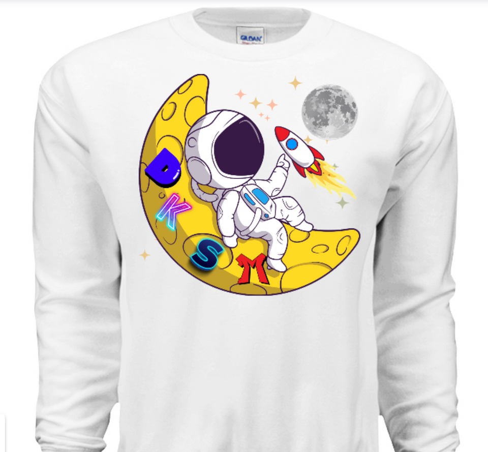 Astronaut holding rocket, sitting on yellow moon with DKSM letters, white sweatshirt.