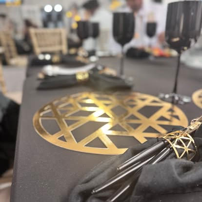 Elegant table set with black tablecloth, golden placemat, black napkins, glasses.