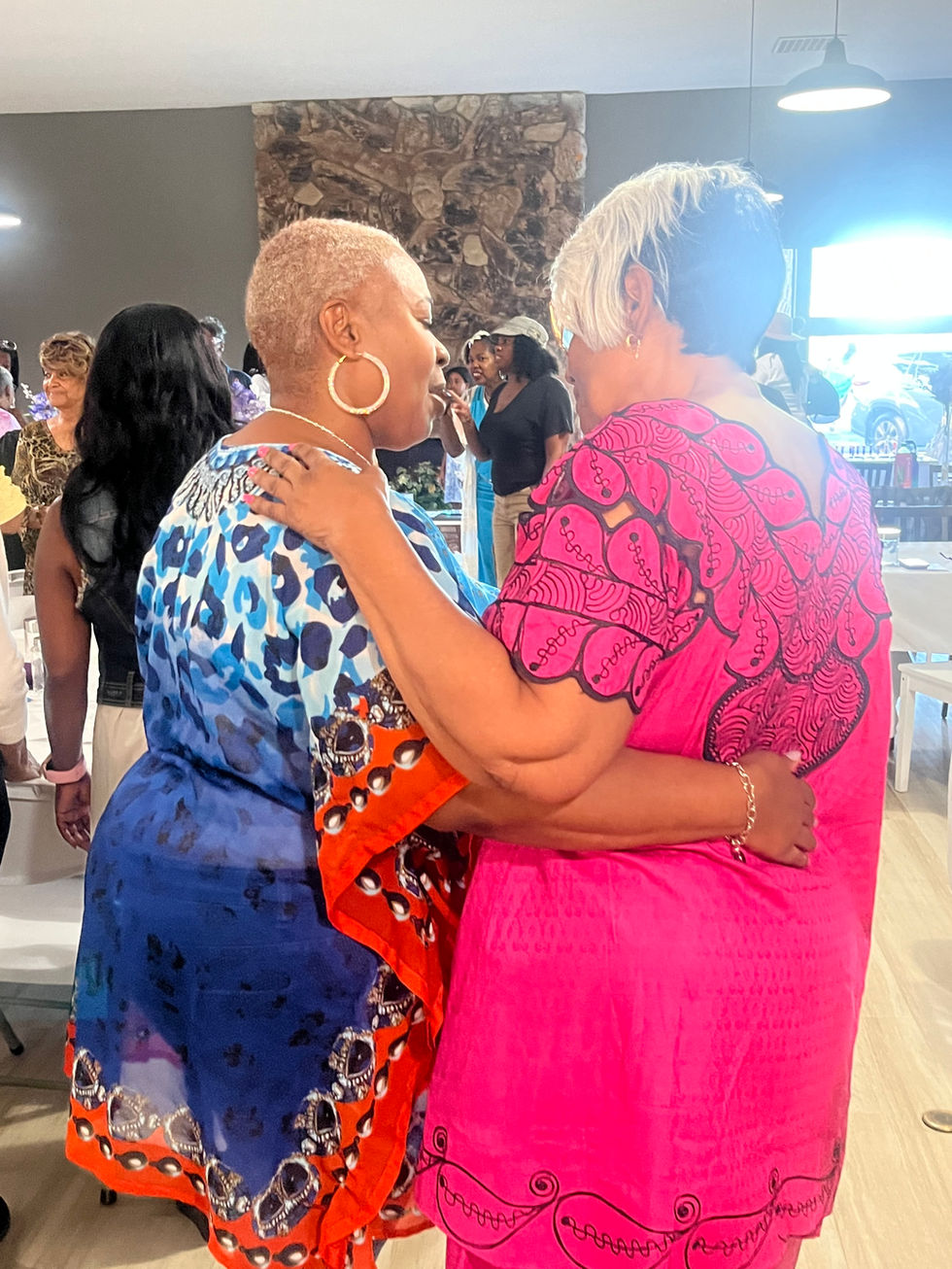 Two women embracing, one in blue patterned dress, other in pink top