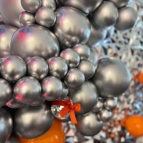 Cluster of shiny silver balloons with one small red-bowed balloon.