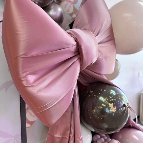 Large pink satin bow among iridescent and light pink balloons.