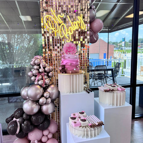Baby shower dessert display with 'Oh Baby' neon sign, pink cakes, balloons.