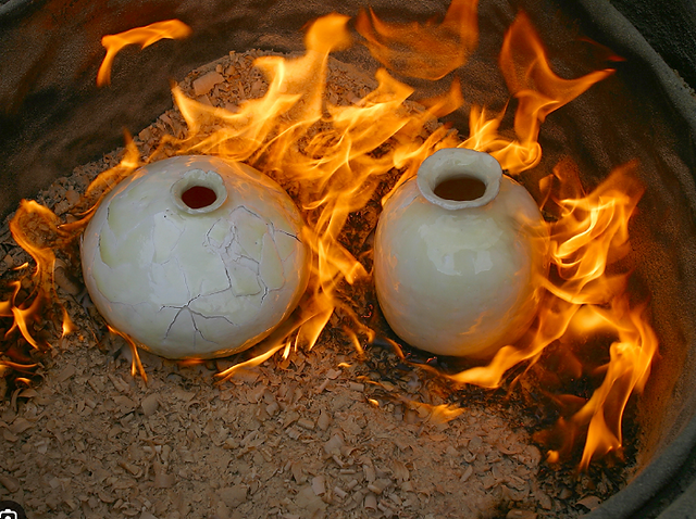 Two ceramic pots firing in a kiln with vibrant flames and heat.