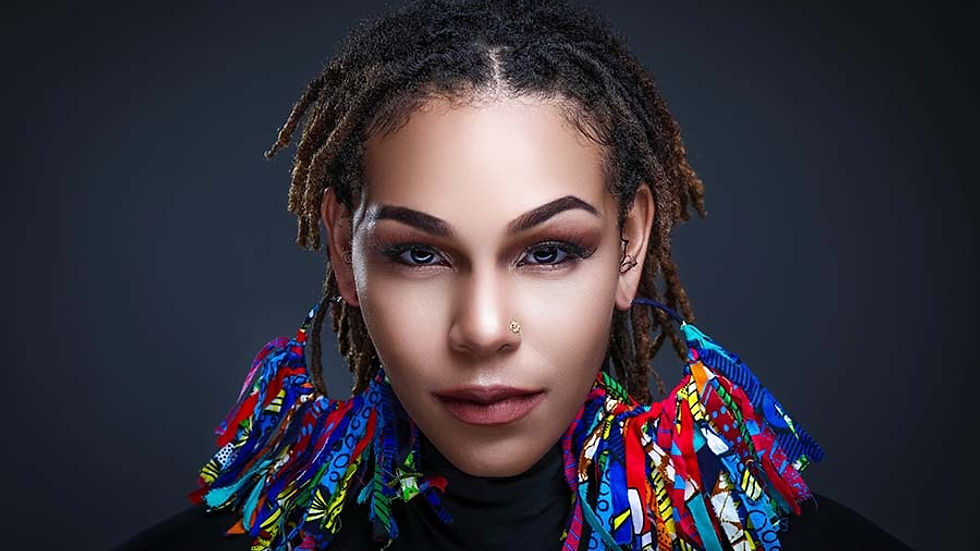 Close-up glam headshot of model with locs, bold makeup, and colorful statement earrings – portfolio image by MooD-ology Photography.