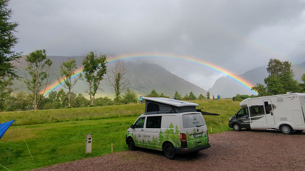 campervans parked under a small but bright rainbow with the Glencoe hills in the background