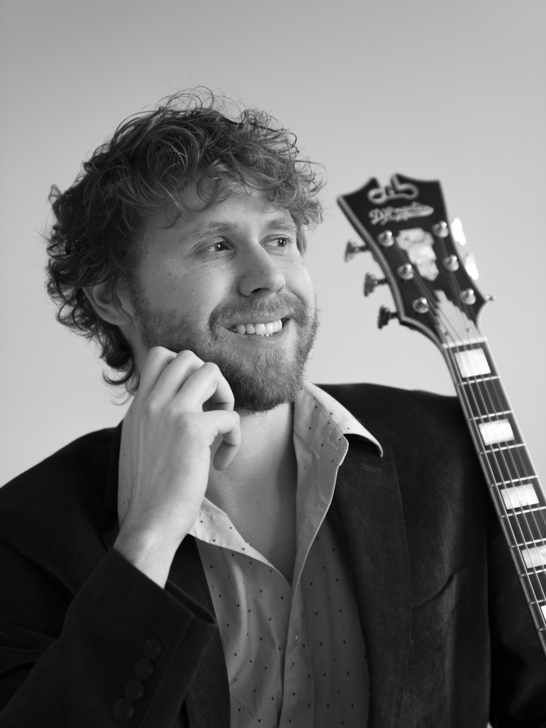 NYC jazz guitarist Hans Luchs smiling beside the headstock of his archtop guitar, black and white