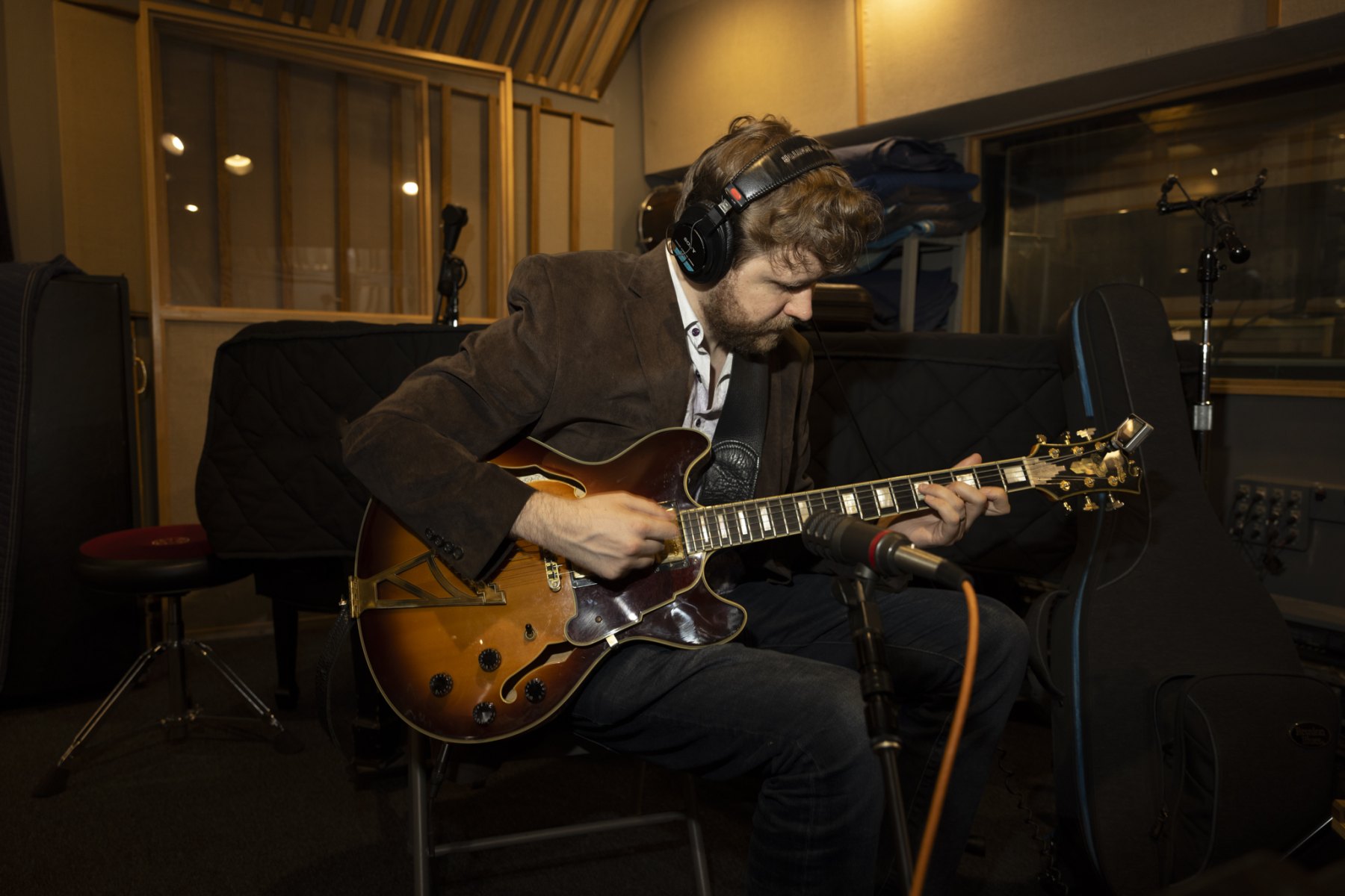 Hans Luchs in headphones recording on his archtop guitar in a wood-panelled studio