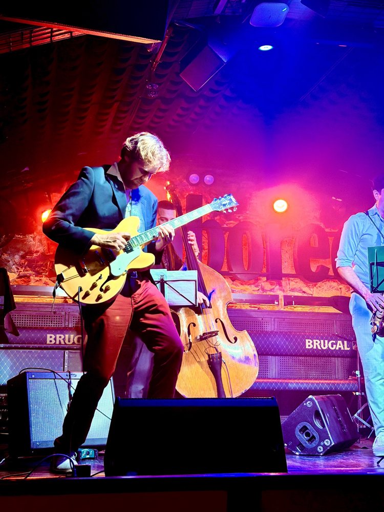 Hans Luchs playing a blonde hollow-body guitar on stage at Jamboree under red and purple lights