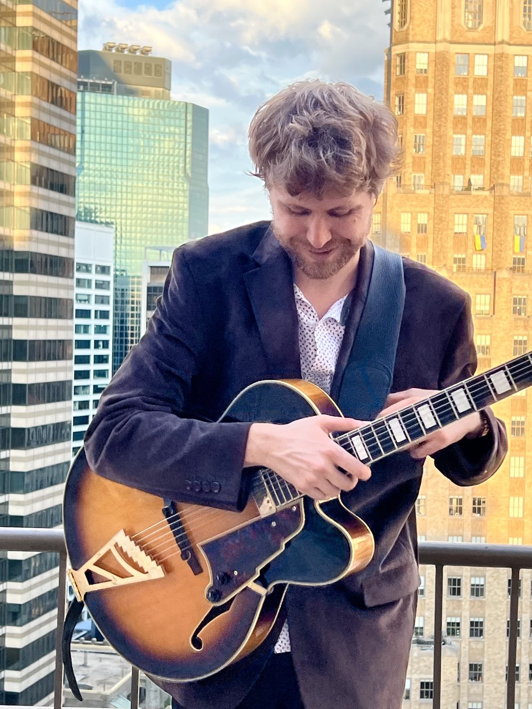 Hans Luchs looking down at the fretboard of his archtop guitar on a Manhattan rooftop