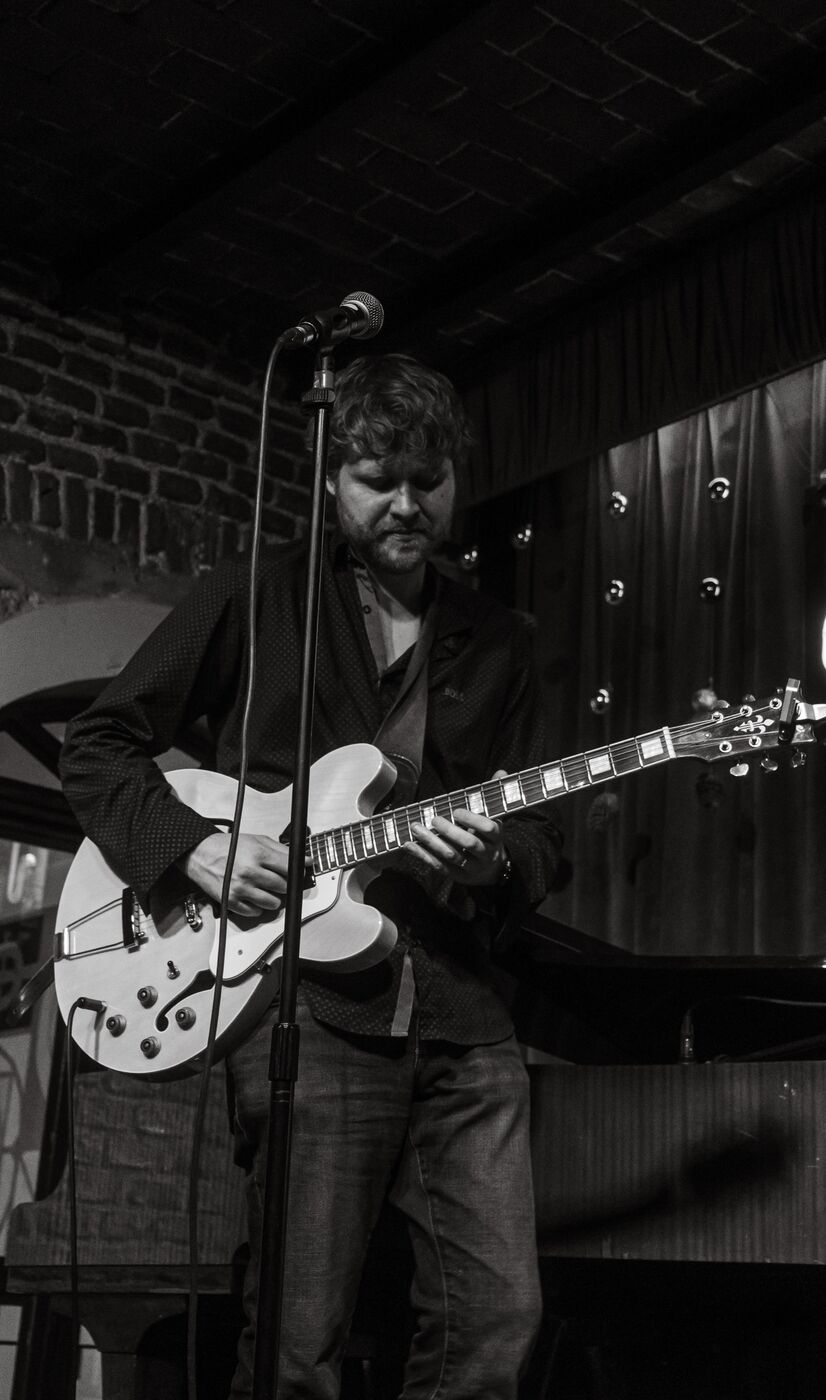 Hans Luchs playing a semi-hollow guitar on stage, black and white