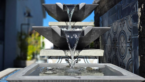 Handcrafted multi-tier concrete water feature with cascading flow, clean lines, and geometric bowls set against tile and stone in an outdoor patio space