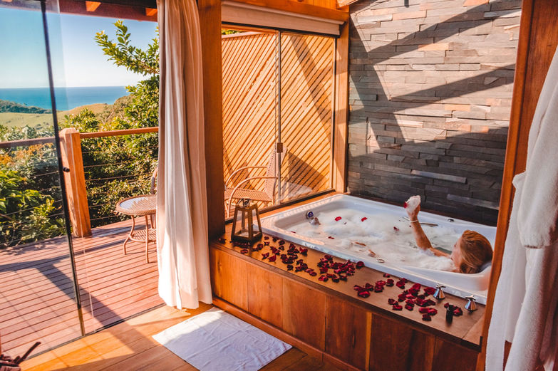 Mulher relaxando na Banheira de Hidromassagem com Vista da Praia do Rosa, detalhe da parede de pedra ferro