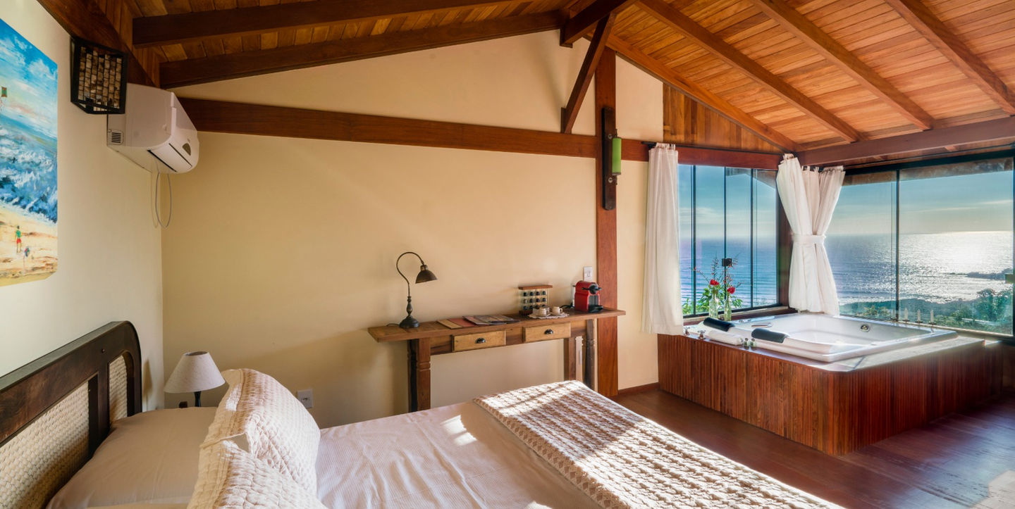 Visão geral do quarto de casal com banheira de hidromassagem, cafeteira Nespresso, Ar condicionado Split e deslumbrante vista da Praia do Rosa no amanhecer