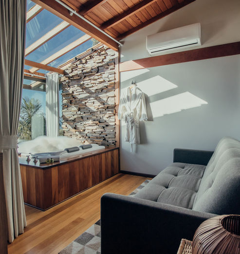 Detalhes da Acomodação com Sofá Cama Confortável, Ar Condicionado Split Inverter, Banheira de Hidromassagem com espuma e Teto de Vidro em um dia ensolarado