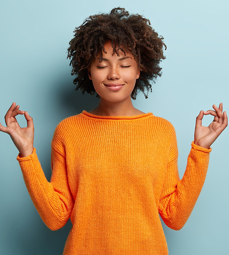 Mindful peaceful Afro American woman meditates indoor, keeps hands in mudra gesture, has e