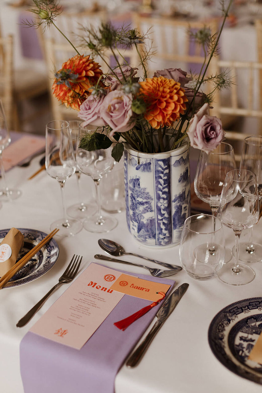 Modern and minimalistic wedding table featuring white table linen, lilac napkins and pastel orange stationery.