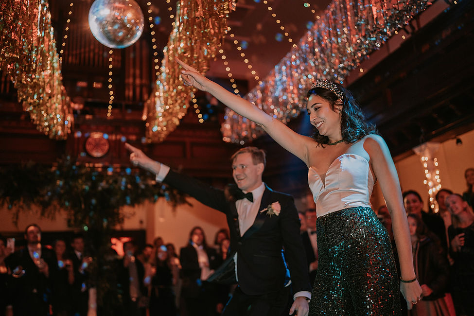 A newly married couple dance their first dance beneath a disco ball and gold streamers, styled by Whole Lotta Love Weddings