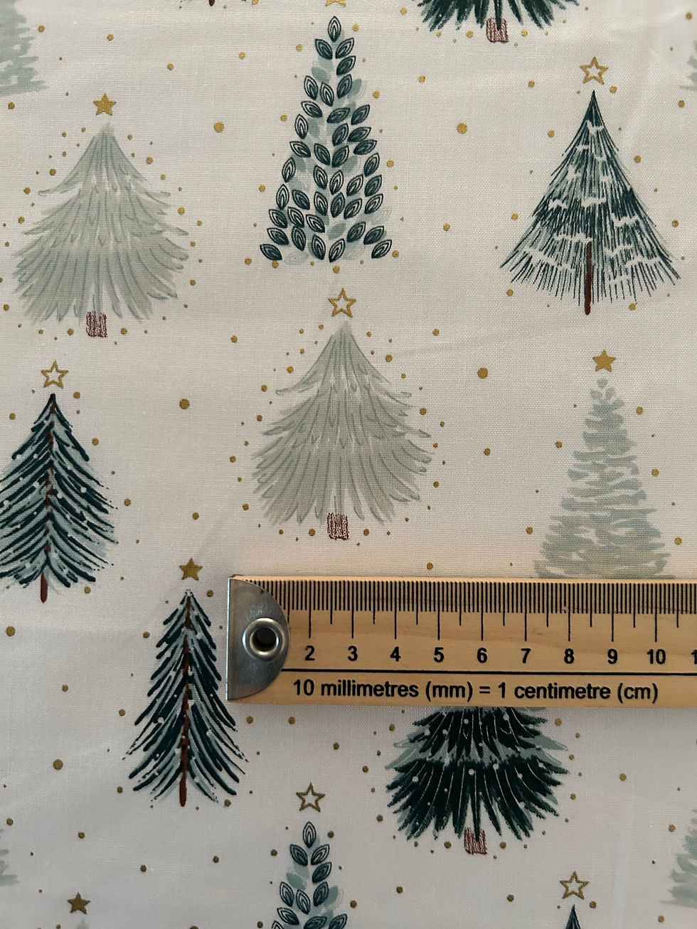 Thumbnail: Christmas tree fabric features different styles of green trees with gold metallic stars and details. Ruler to show print size