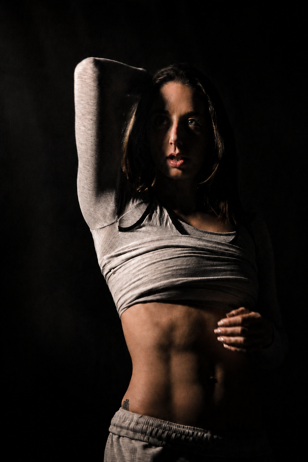 Donna con fisico tonico in posa fitness, illuminata da luce cinematica, per rappresentare i cambiamenti estetici ottenibili con l’allenamento funzionale.
