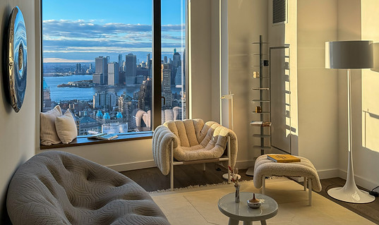 Sunlit modern sitting area in Downtown Brooklyn residence with sculptural armchairs, skyline views, and layered neutral textures. Designed by HOLM Interior Design.