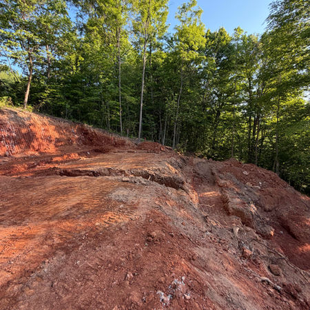 Cleared mountain homesite with fresh grading work surrounded by mature hardwood trees and scenic wooded views.