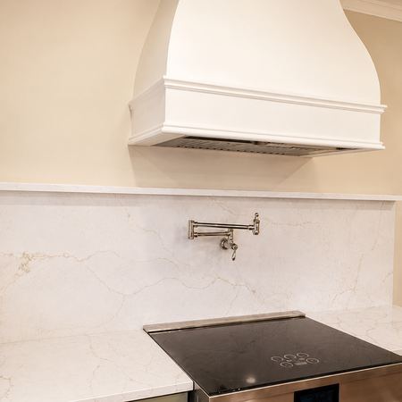 Elegant custom range hood with quartz backsplash and professional-style induction range.