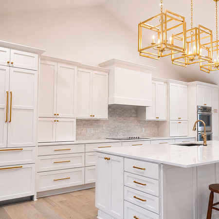 Elegant open-concept kitchen featuring custom white cabinetry, expansive quartz island, brushed gold fixtures, and oversized geometric pendant lighting beneath vaulted ceilings.