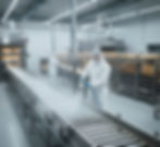 Operario de Crioblast en Quito con traje blanco de bioseguridad aplicando limpieza criogénica en una cinta transportadora de fábrica de pan. La imagen destaca la higiene y eficiencia, optimizando la producción y la seguridad alimentaria en entornos de panadería.