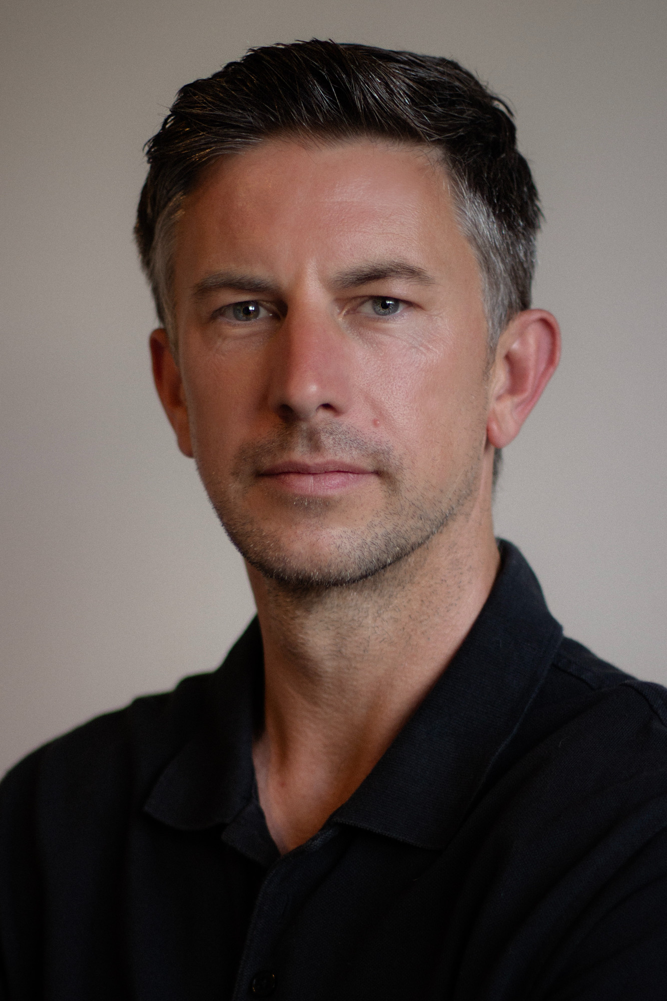 Portrait of a man in a black Levi's polo with arms crossed, looking at camera against a plain gray background.