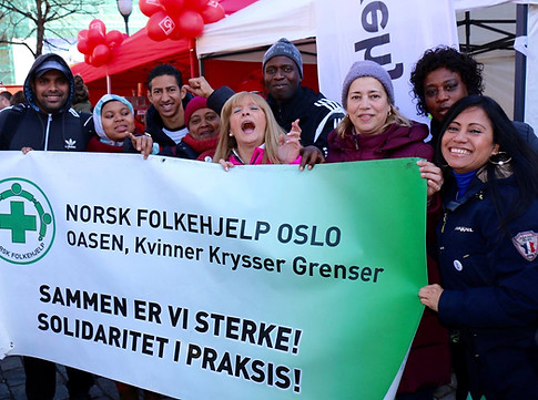 En gruppe engasjerte mennesker holder opp et banner som sier "Norsk Folkehjelp Oslo, Kvinner Krysser Grenser, Sammen er vi sterke! Solidaritet i praksis!"