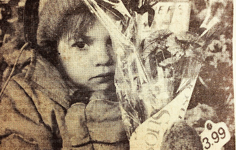 Image of the author as a serious  3 year-old, bundled in winter clothes holding a bouquet