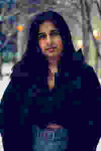 Photo of a woman wearing a black coat and blue jeans standing outside in the snow fall