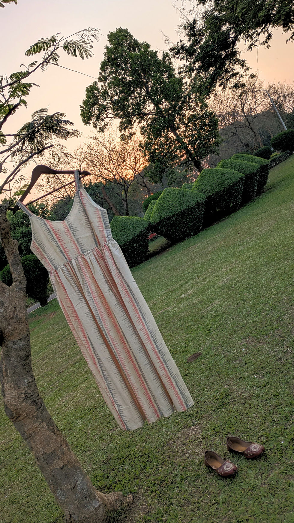 Thumbnail: Strappy handloom cotton maxi dress with soft vertical stripe pattern hanging outdoors in natural light