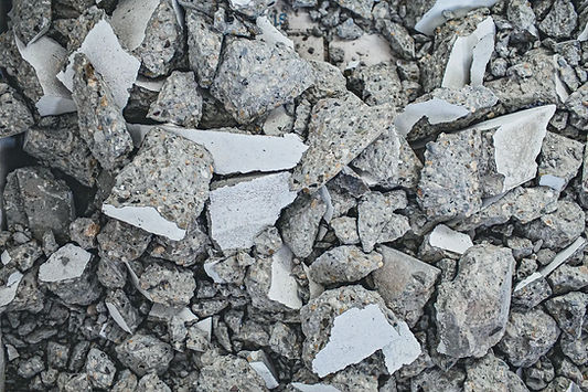 A close-up view of crushed concrete rubble and broken concrete chunks, with irregular gray rocks and white fragments scattered in a pile.