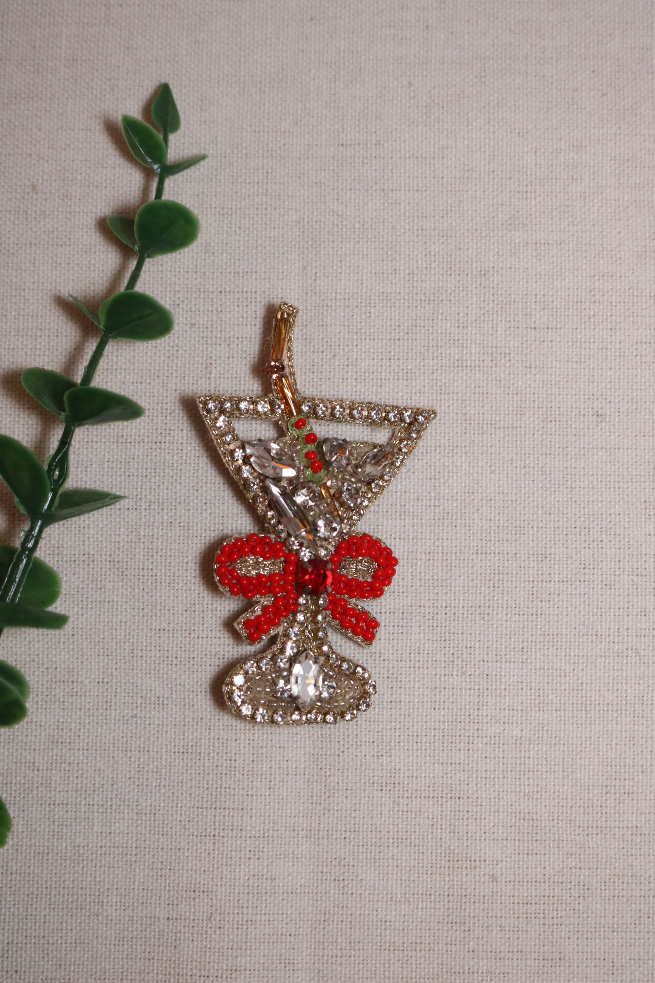 Handgemaakte broche in de vorm van een cocktailglas, gedecoreerd met zilverkleurige kristallen, een rode kralenstrik