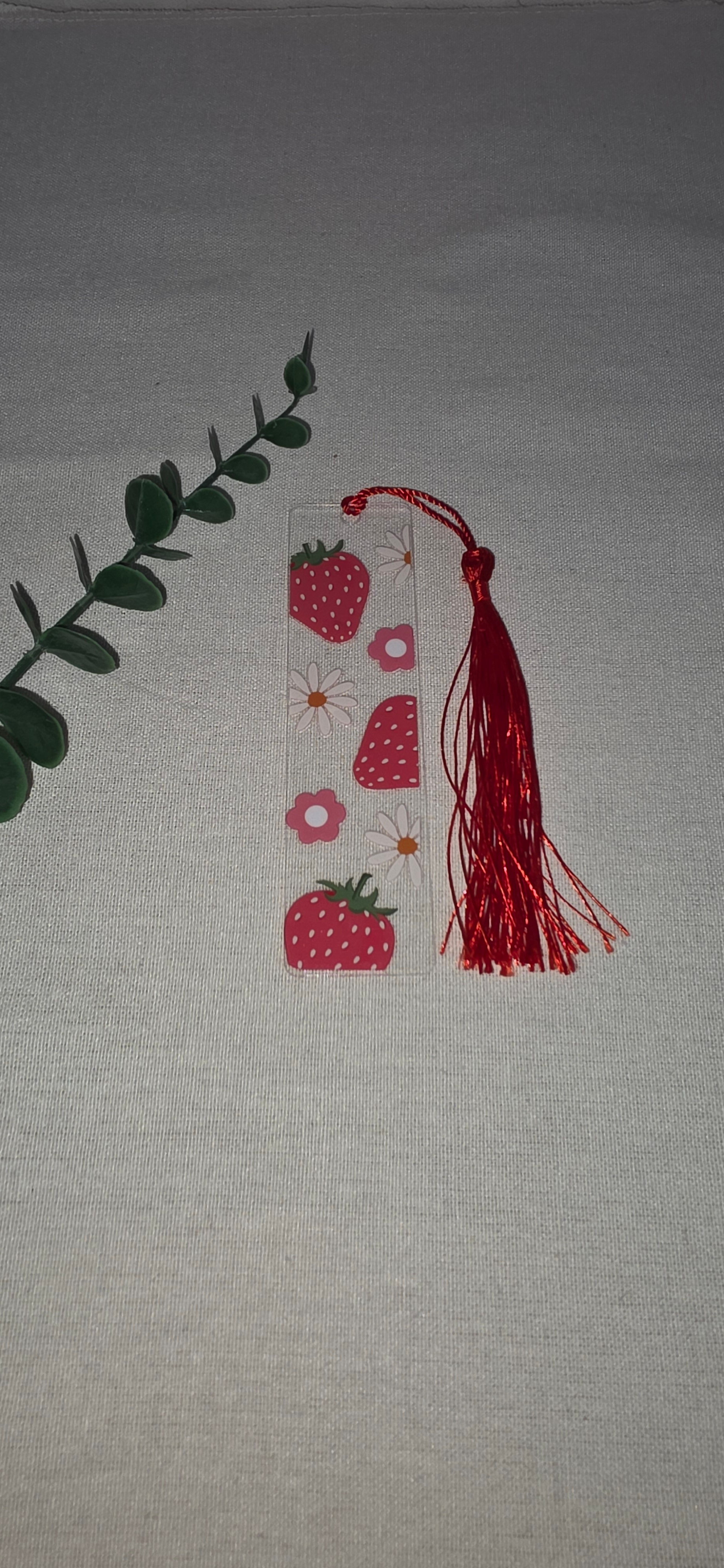 Acryl boekenlegger met vrolijke print van rode aardbeien en witte en rode madeliefjes, afgewerkt met rood kwastje