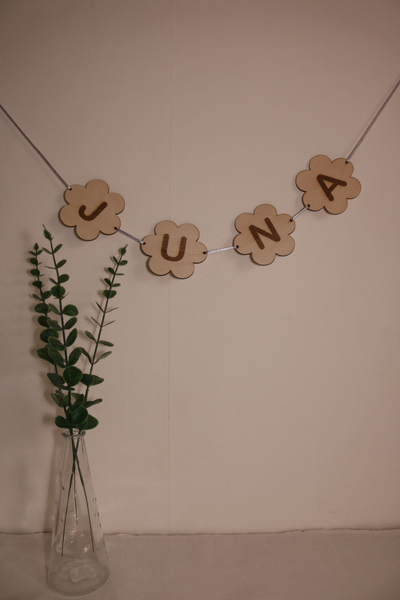 Gepersonaliseerde houten naamslinger met bloemenvormen en gegraveerde letters, hangend aan een muur