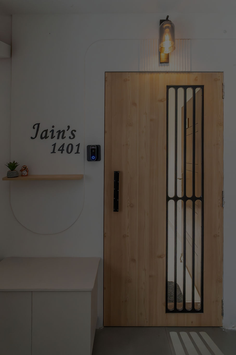 This 3BHK residential interior project is designed in a soft contemporary style, blending pastel hues, warm wooden finishes, and clean modern detailing to create a calm yet refined living environment. The design approach focuses on balancing functionality with subtle elegance, ensuring every space feels open, inviting, and thoughtfully curated.

The living room features a neutral sofa palette enhanced with mustard and textured cushions, a custom floating TV unit with wooden accents, and vertical fluted detailing that adds depth to the walls. Warm pendant lighting and concealed cove lights introduce layered illumination, enhancing the overall ambience.

An arched transition between spaces softens the layout, while the dining area incorporates upholstered green chairs with gold accents, creating a sophisticated contrast against the neutral backdrop. The carefully designed console and mirror wall treatment enhance spatial perception while maintaining minimalism.

The bedrooms showcase pastel blue wall panelling combined with nature-inspired wallpaper panels, rattan wardrobe shutters, and warm wood cladding for a cozy aesthetic. Customized study units with open shelving and ergonomic seating create functional work-from-home spaces without compromising design harmony.

The modular kitchen follows a modern L-shaped layout with handle-less cabinetry, white subway tile backsplash, under-cabinet lighting, and full-height wooden overhead units that add warmth and texture.

A dedicated pooja niche with backlit curved detailing becomes a serene spiritual focal point, integrating traditional elements within a contemporary setting.

This project reflects a complete turnkey interior solution — combining space planning, custom furniture design, layered lighting, and material harmony to create a refined, modern family home.