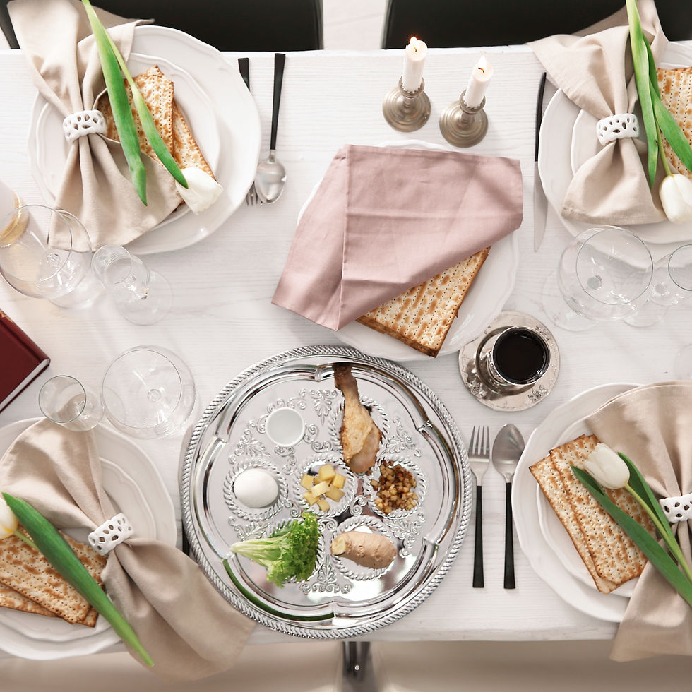 Elegant Passover seder table with matzah, tulips, candles, silver tray of symbolic foods, and wine glasses on a white table.