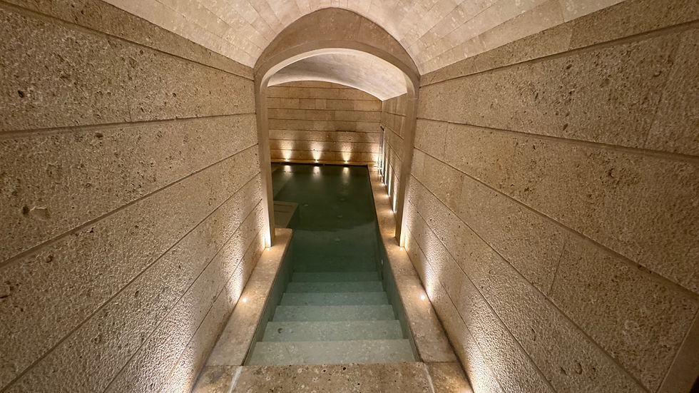 Stone stairway leads to an underground pool. Warm lighting highlights textured stone walls, creating a tranquil, ancient ambiance.