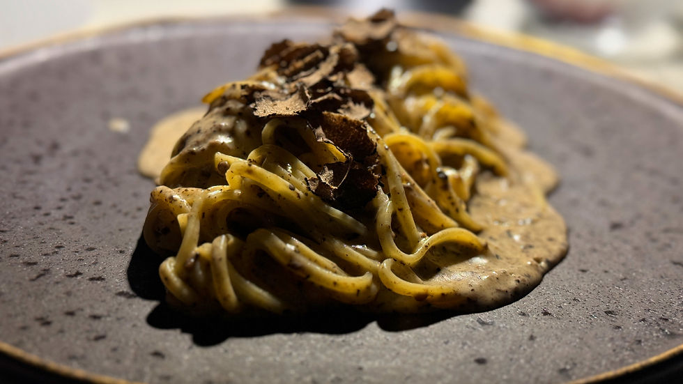 Close-up of pasta with creamy sauce and shaved truffles on a dark speckled plate. Warm, inviting mood in soft lighting.