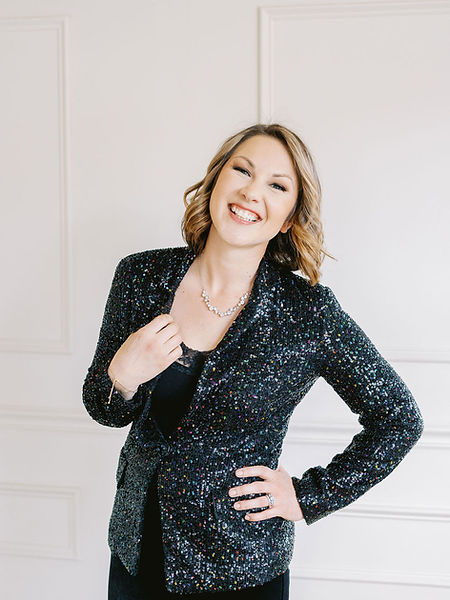Jenna in a black sequin blazer, grinning against a white wall.