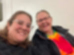Two women smiling at an event, one in a colorful tie-dye shirt.