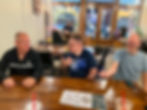 Three men using sign language while sitting at a table.