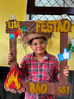 Menino com camisa quadriculada e chapéu de palha tirando foto para registrar a Festa Julina.