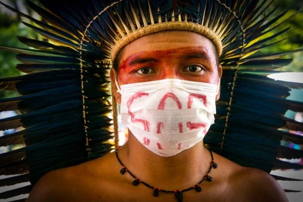 Homem indígena com máscara escrito SOS - covid Amazônia