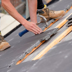 Roofer installing slate tiles with a hammer on a new roof