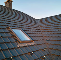 Modern dark tiled roof with a skylight and chimney.